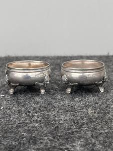 Pareja de saleros de plata de tres patas con figuras de arpías.
    