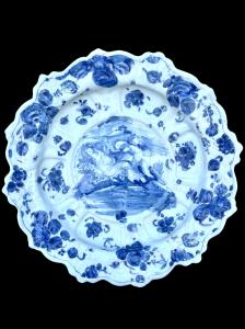 Grande piatto in maiolica  a bordo lobato in monocromia turchina a sfondo berettino con decoro a personaggi con sfondo agreste e architetture.Marca lanterna.Savona.