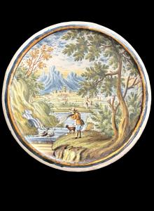 Tondo de mayólica que representa a un cazador disparando a la fauna en un entorno rural con arquitectura. Castelli d'Abruzzo.